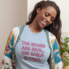 Woman wearing a light blue t-shirt with the text 'The boobs are real, the smile is fake.' printed in pink on the front.