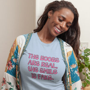 Woman wearing a light blue t-shirt with the text 'The boobs are real, the smile is fake.' printed in pink on the front.