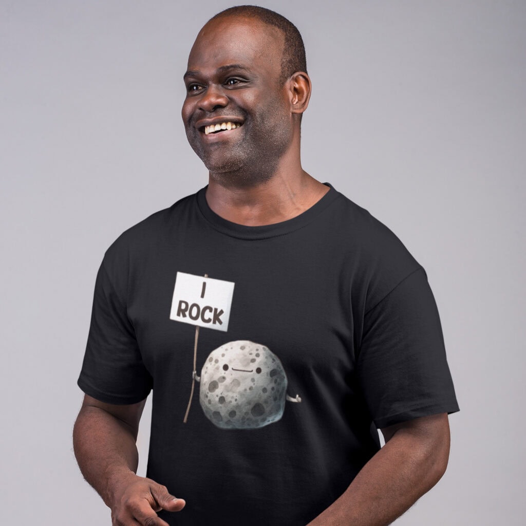 Man smiling while wearing a black t-shirt. The shirt has an image of a grey rock that is holding a sign. The sign says 'I Rock.' The image is printed on the front of the shirt.