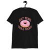 Black t-shirt that has an image of a donut with pink icing and sprinkles and the text 'Eat more hole foods' printed on the front.