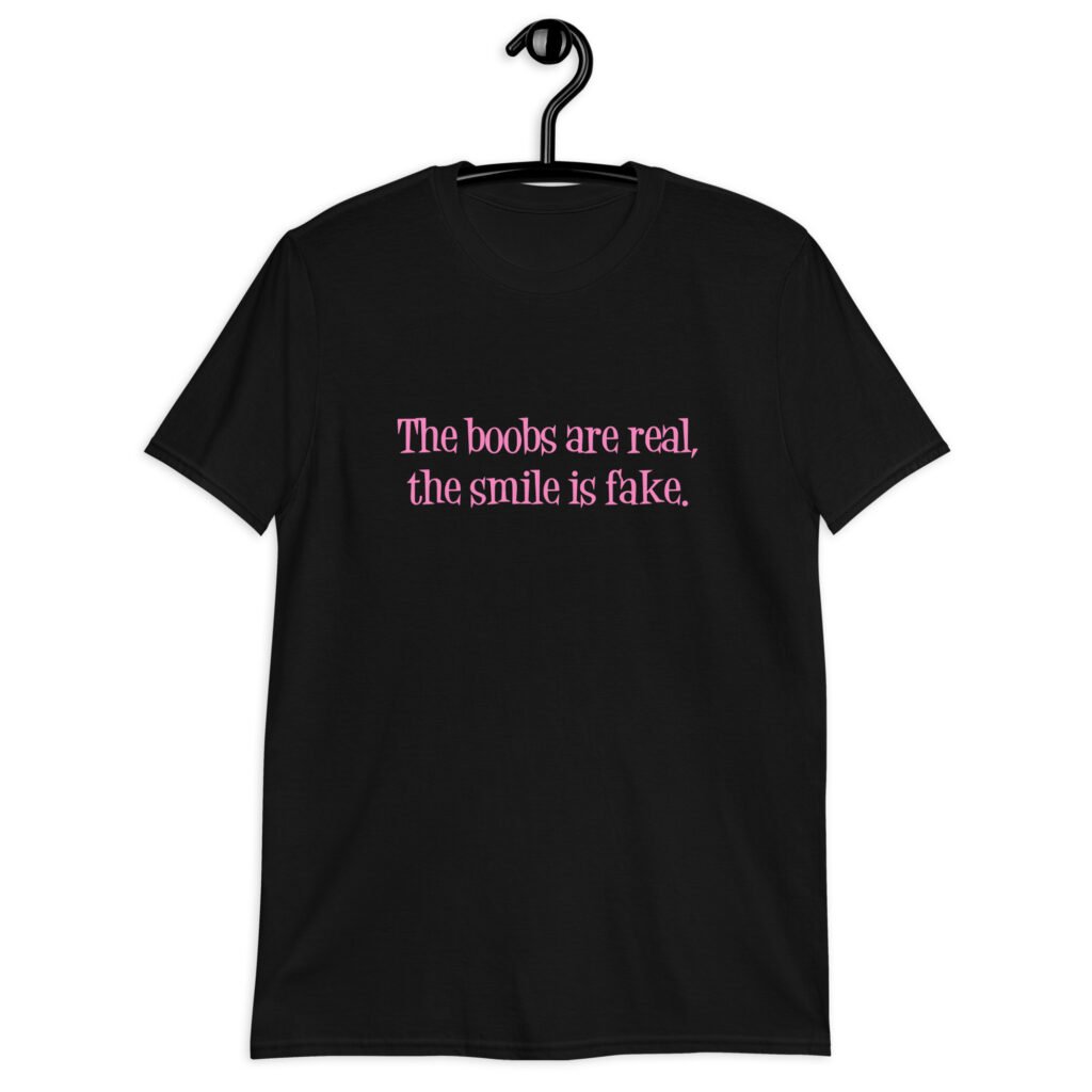 Black t-shirt with the text 'The boobs are real, the smile is fake.' printed in pink on the front.