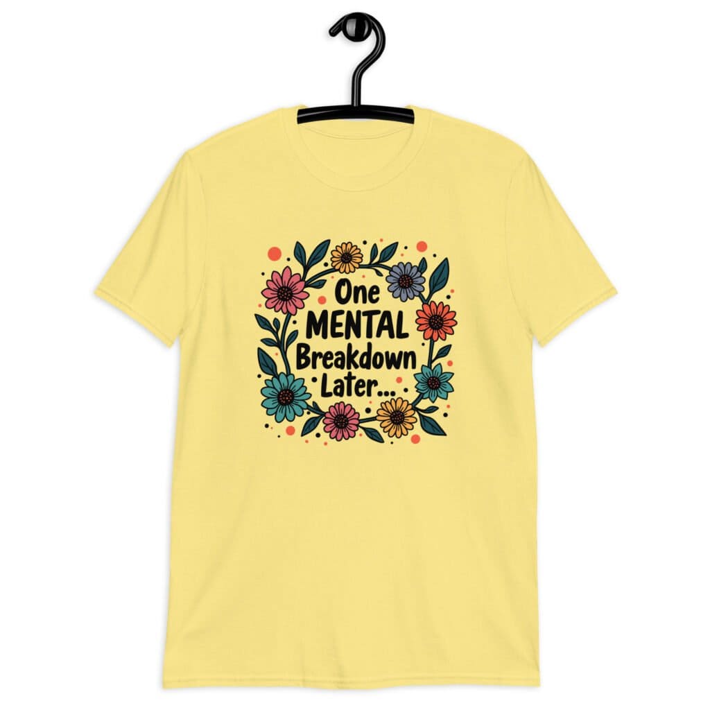 Cornsilk yellow t-shirt with a multi color floral wreath design printed on the front. The words 'One mental breakdown later...' are printed in the center of the wreath.