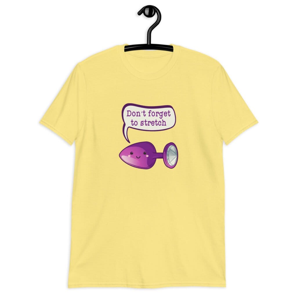Cornsilk yellow t-shirt that has image of a purple anal plug with a smile face. There is a speech bubble above with the words 'Don't forget to stretch'. The graphics are printed on the front of the shirt.