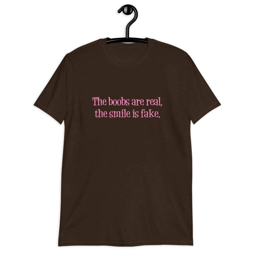 Dark chocolate brown t-shirt with the text 'The boobs are real, the smile is fake.' printed in pink on the front.