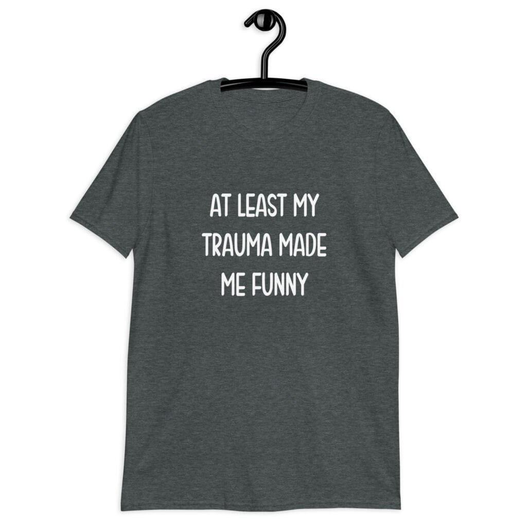 Dark heather grey t-shirt with the text 'At least my trauma made me funny' printed on the front.