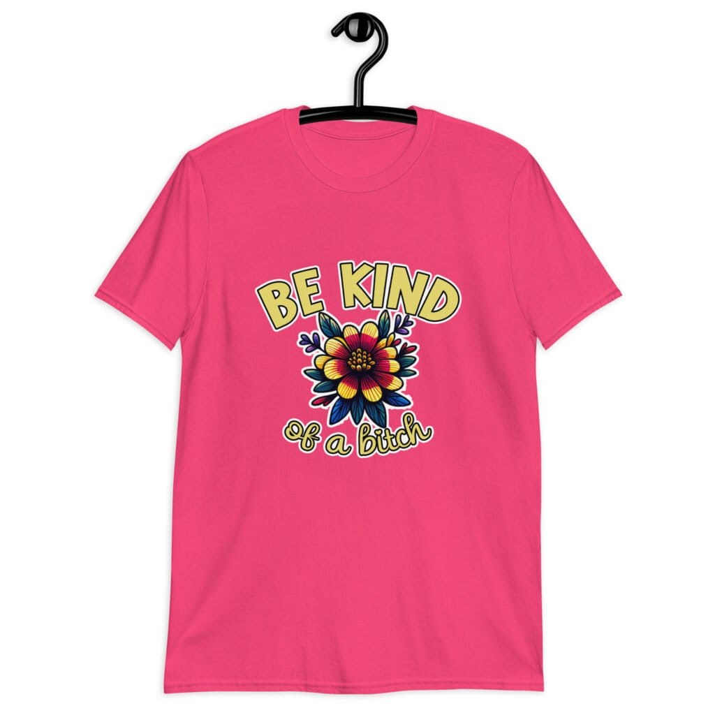 Heliconia pink t-shirt with an image of a flower and the words Be kind above the flower in yellow bold block font. The words Of a bitch are smaller in script font under the flower. The design is printed on the front of the shirt.