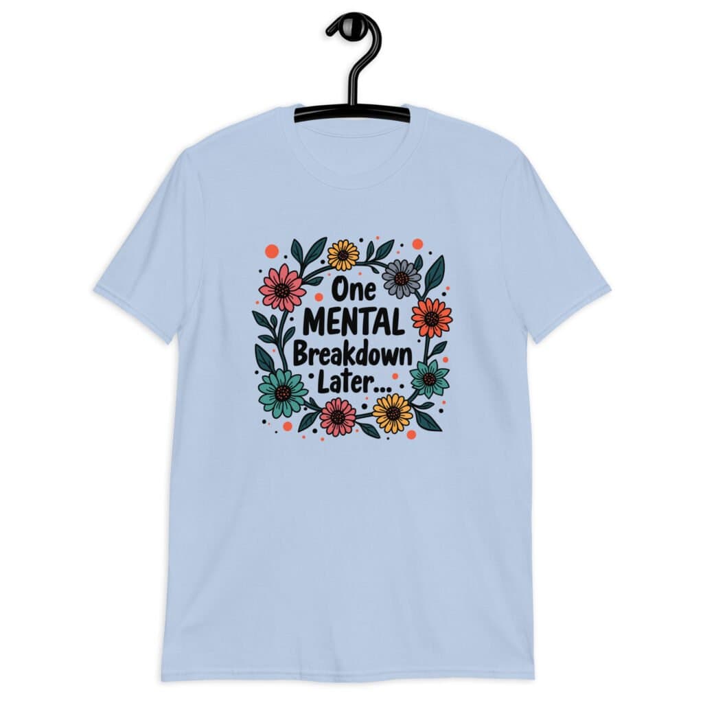 Light blue t-shirt with a multi color floral wreath design printed on the front. The words 'One mental breakdown later...' are printed in the center of the wreath.