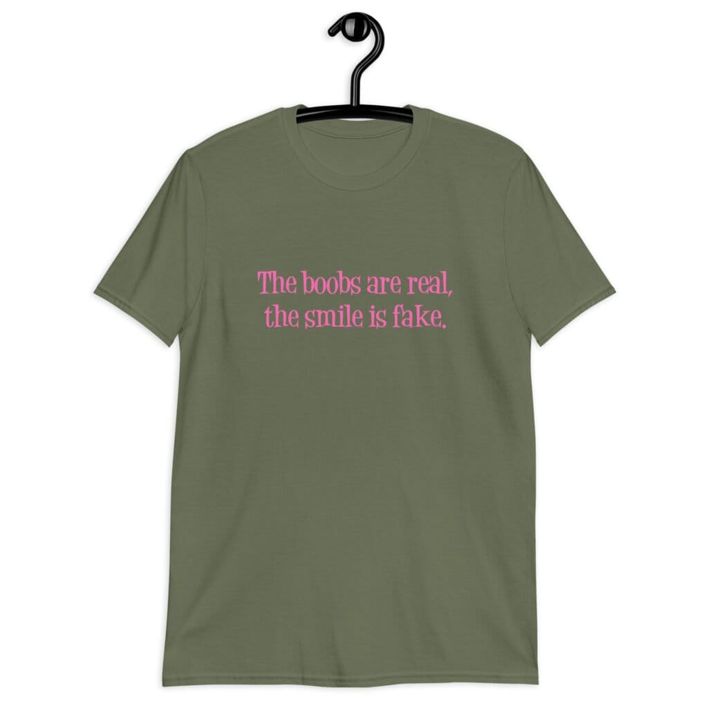 Military green t-shirt with the text 'The boobs are real, the smile is fake.' printed in pink on the front.