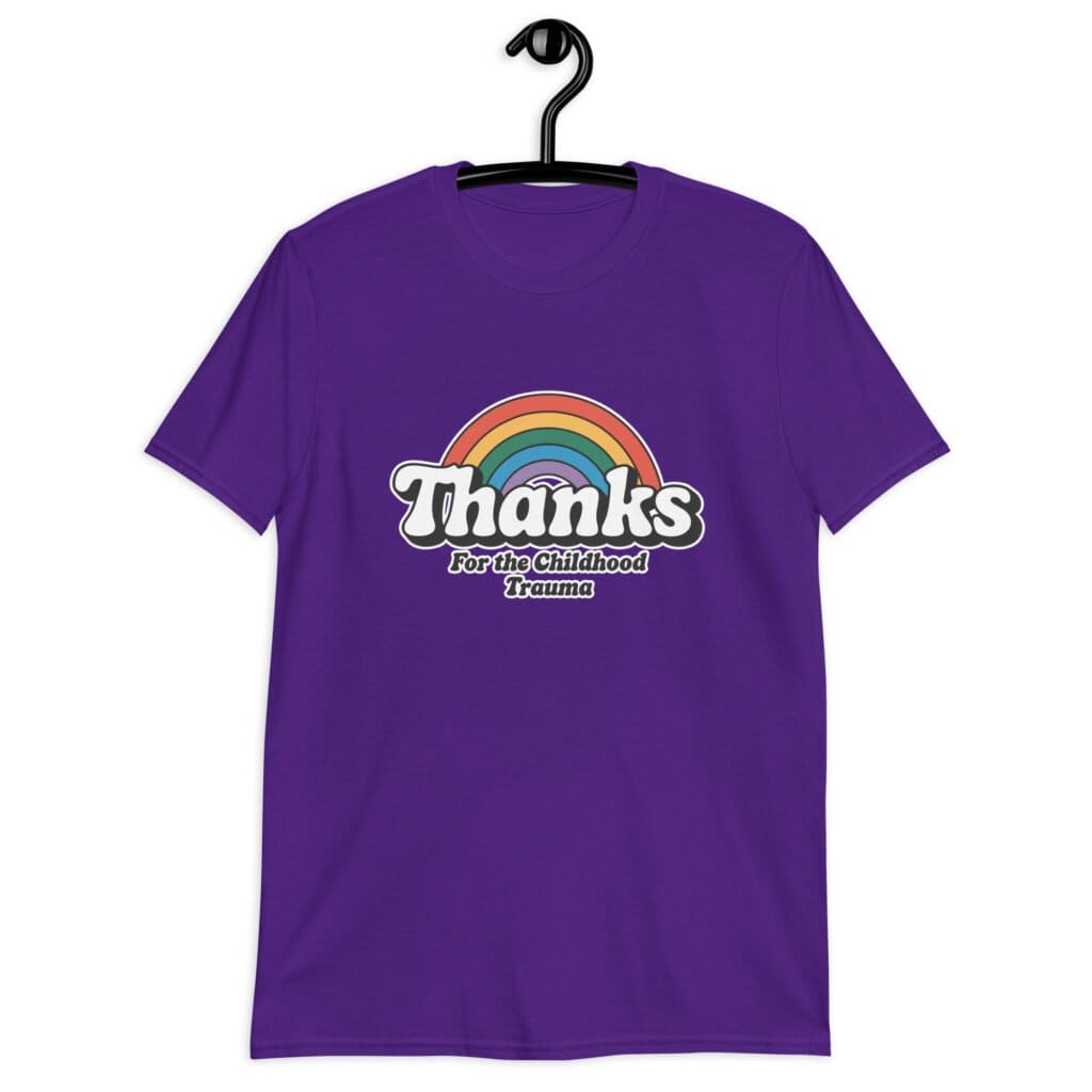 Purple t-shirt with an image of a rainbow and the words 'Thanks for the childhood trauma' printed on the front. The word Thanks is large and the rest of the words are smaller under.