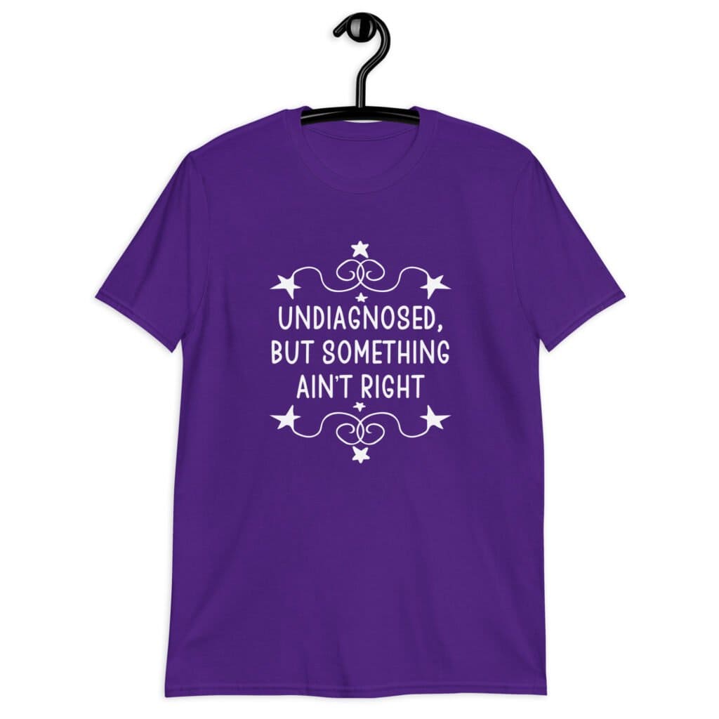 Purple t-shirt with the phrase 'Undiagnosed, but something ain't right 'printed on the front. The text is white and has a star graphic embellishment around the words.