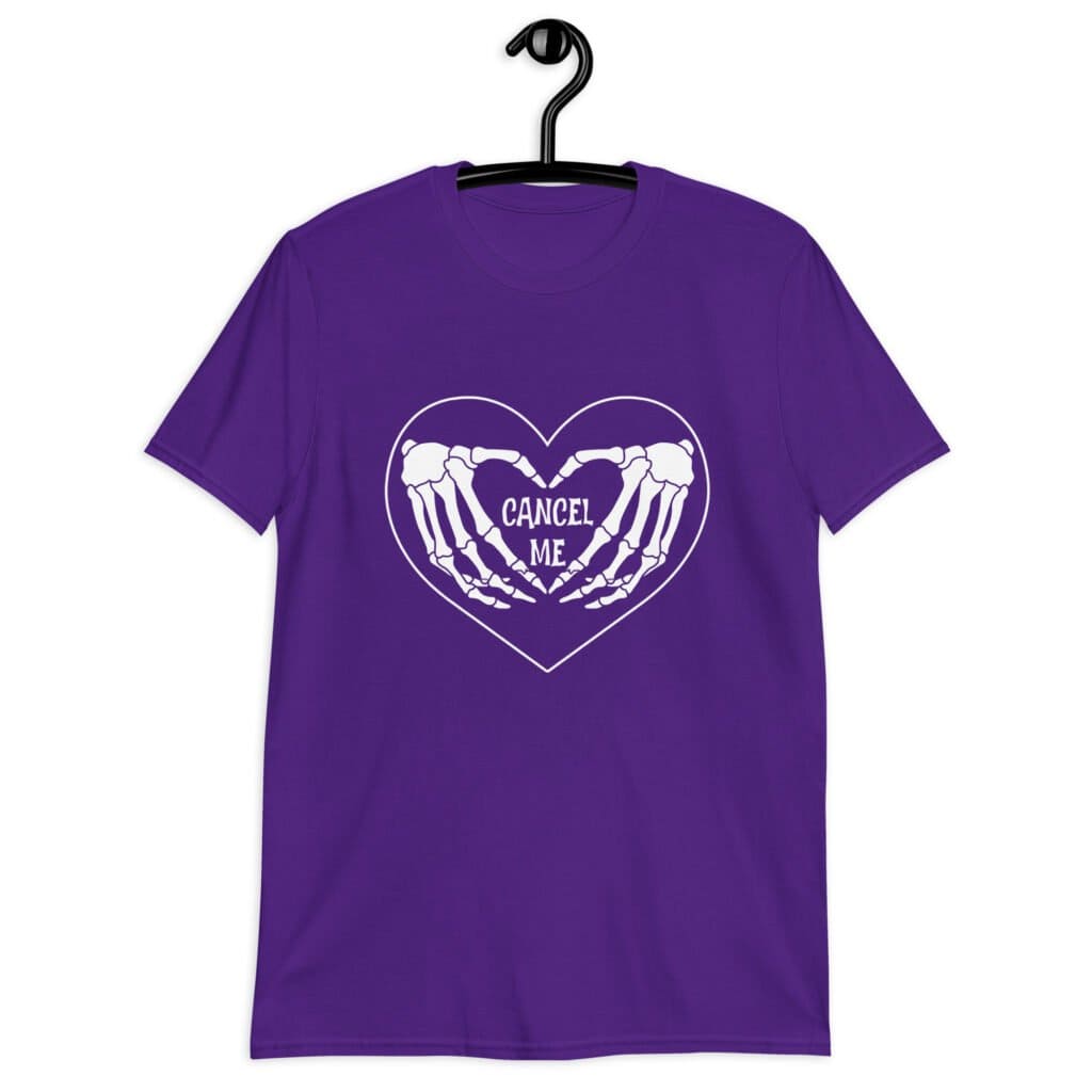 Purple t-shirt with a heart and skeleton hands making a heart shape printed on the front. The words 'Cancel Me' are inside of the heart.