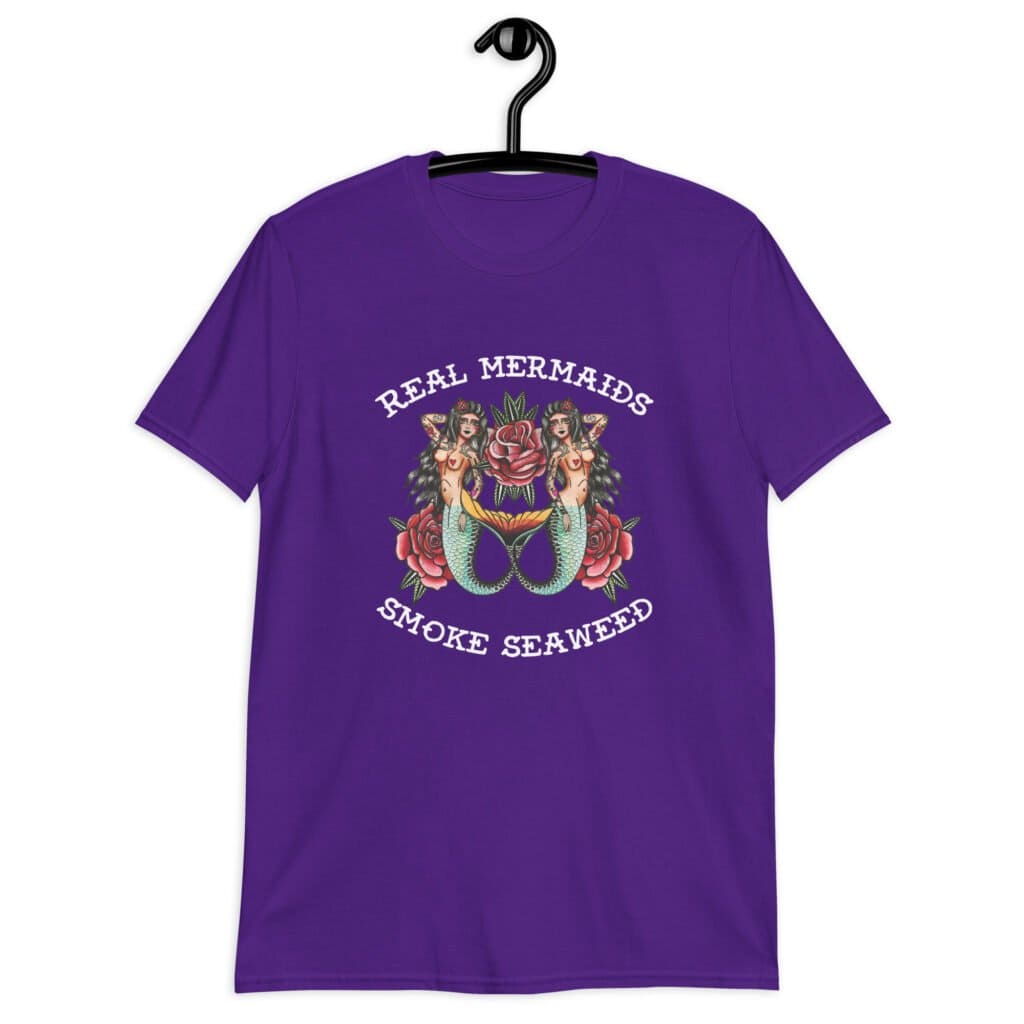 Purple t-shirt with image of 2 mermaids and the text 'Real mermaids smoke seaweed' printed on the front.