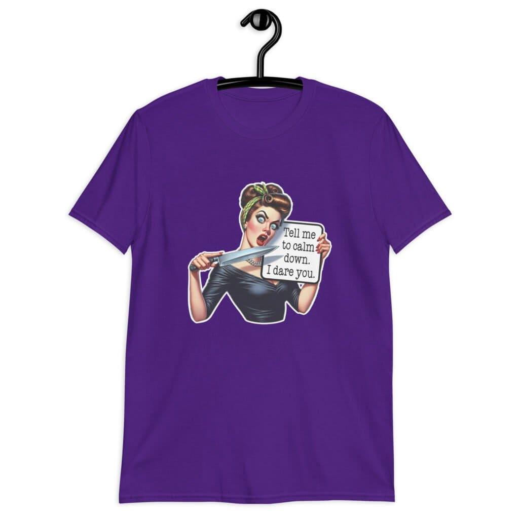 Purple t-shirt that has a graphic of an angry looking retro woman holding a knife and a sign. The sign says 'Tell me to calm down. I dare you.' The graphic is printed on the front of the shirt.