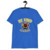 Royal blue t-shirt with an image of a flower and the words Be kind above the flower in yellow bold block font. The words Of a bitch are smaller in script font under the flower. The design is printed on the front of the shirt.
