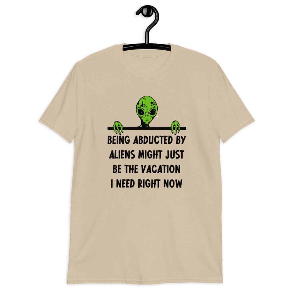 Sand color alien abduction joke t-shirt with image of an alien and the words 'Being abducted by aliens might just be the vacation I need right now' printed on the front.