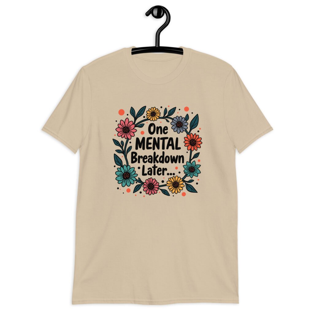 Sand color t-shirt with a multi color floral wreath design printed on the front. The words 'One mental breakdown later...' are printed in the center of the wreath.