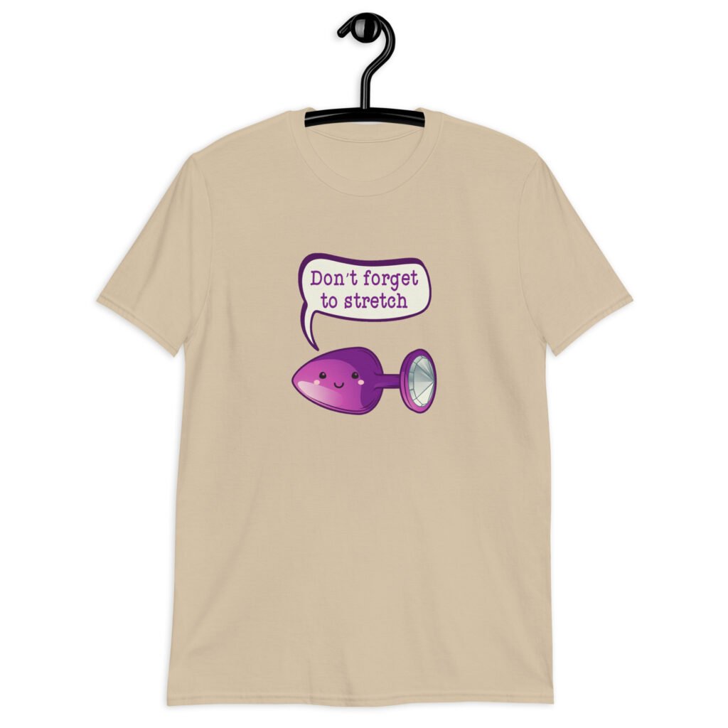 Sand color t-shirt that has image of a purple anal plug with a smile face. There is a speech bubble above with the words 'Don't forget to stretch'. The graphics are printed on the front of the shirt.