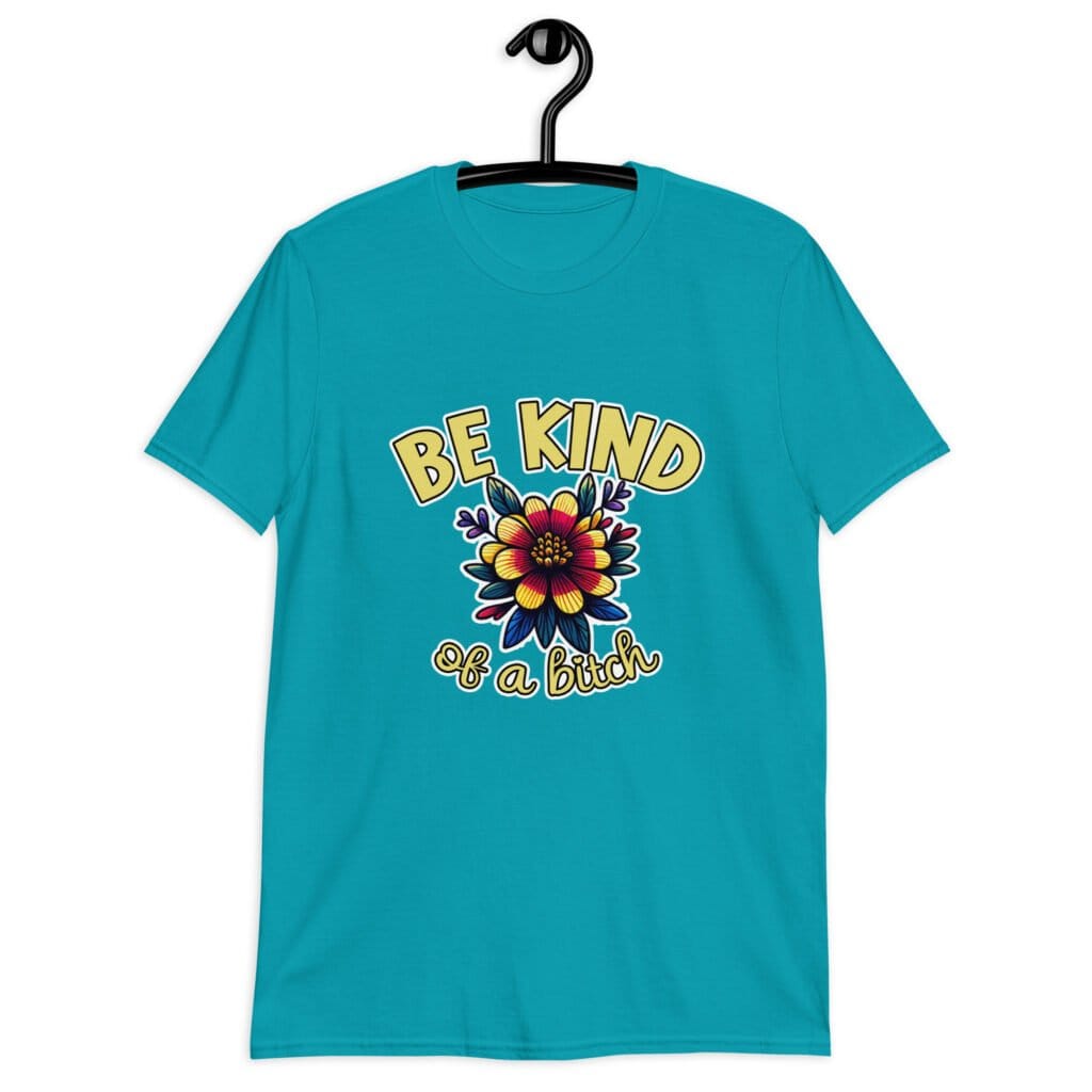 Tropical blue t-shirt with an image of a flower and the words Be kind above the flower in yellow bold block font. The words Of a bitch are smaller in script font under the flower. The design is printed on the front of the shirt.