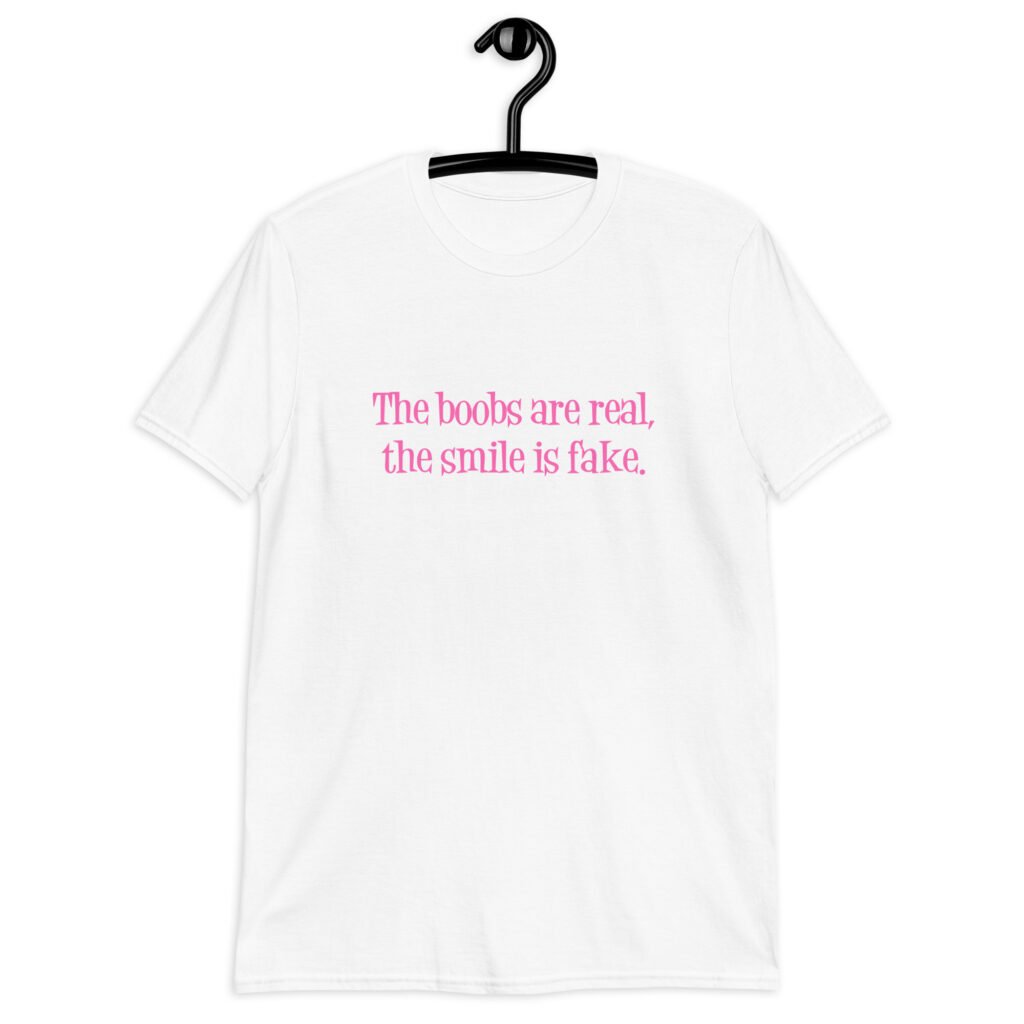White t-shirt with the text 'The boobs are real, the smile is fake.' printed in pink on the front.