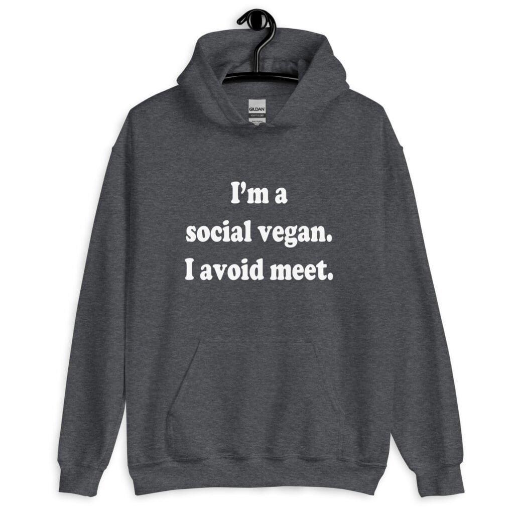 Dark heather grey hoodie sweatshirt with the pun phrase 'I'm a social vegan. I avoid meet.' printed on the front.