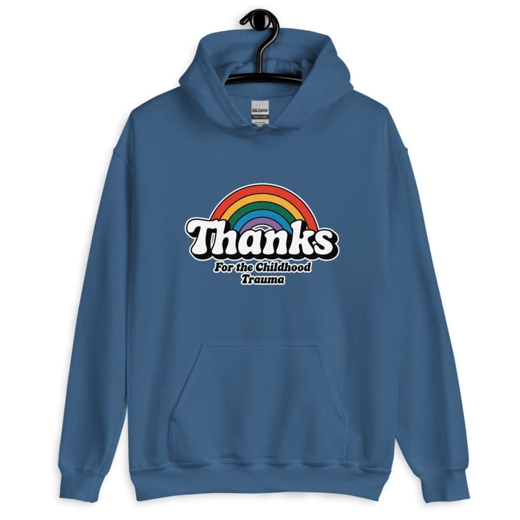 Indigo blue hoodie sweatshirt with an image of a rainbow and the words 'Thanks for the childhood trauma' printed on the front. The word Thanks is large and the rest of the words are smaller under.