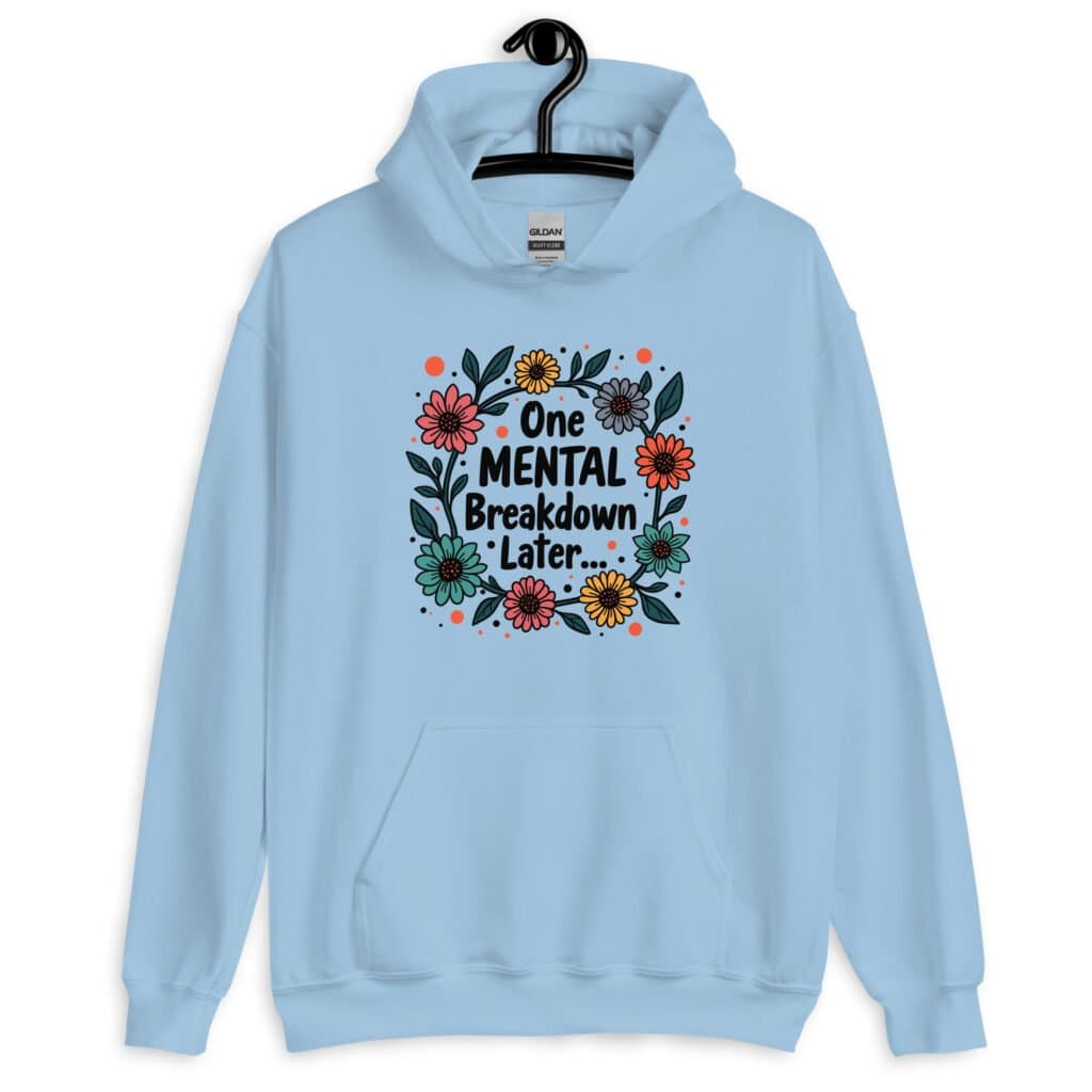 Light blue hoodie sweatshirt with a multi color floral wreath design printed on the front. The words 'One mental breakdown later...' are printed in the center of the wreath.
