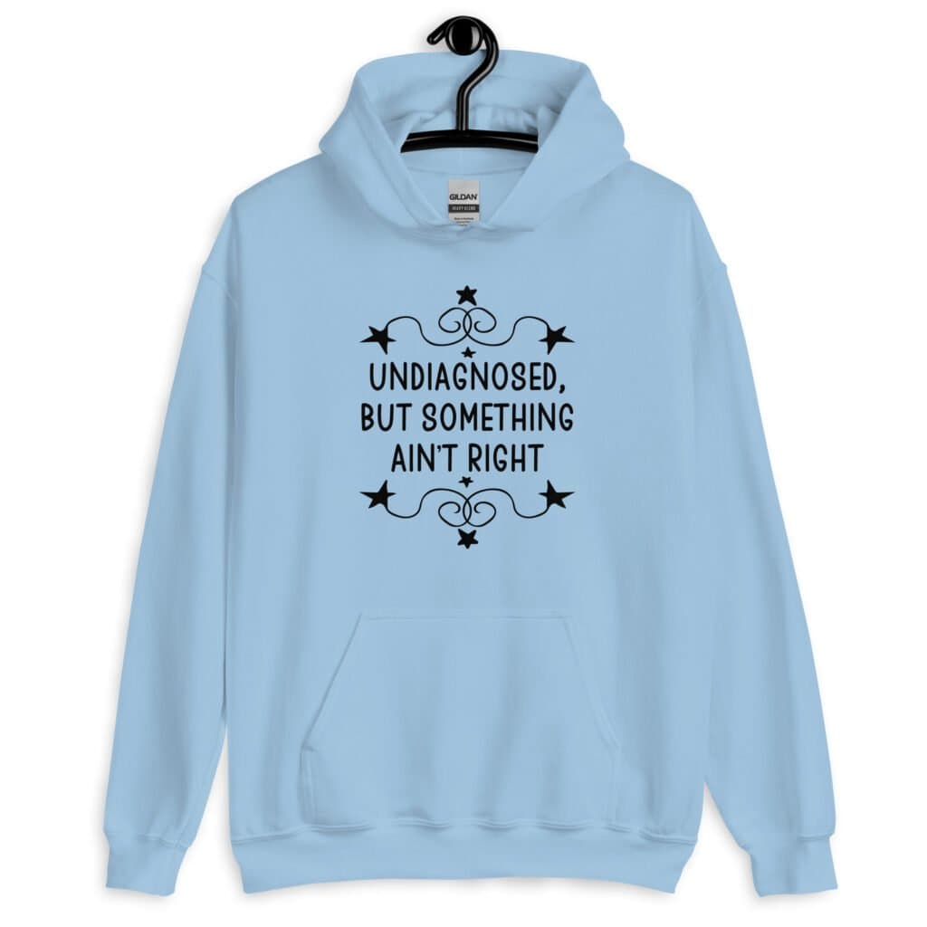 Light blue hoodie sweatshirt with the phrase 'Undiagnosed, but something ain't right 'printed on the front. The text is black and has a star graphic embellishment around the words.