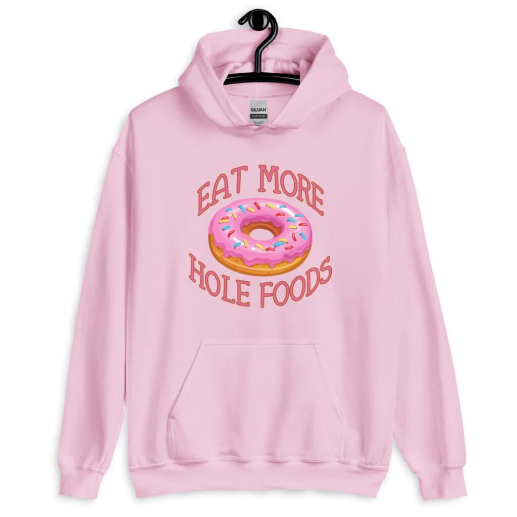 Light pink hoodie sweatshirt with an image of a donut with pink icing and sprinkles and the text 'Eat more hole foods' printed on the front.