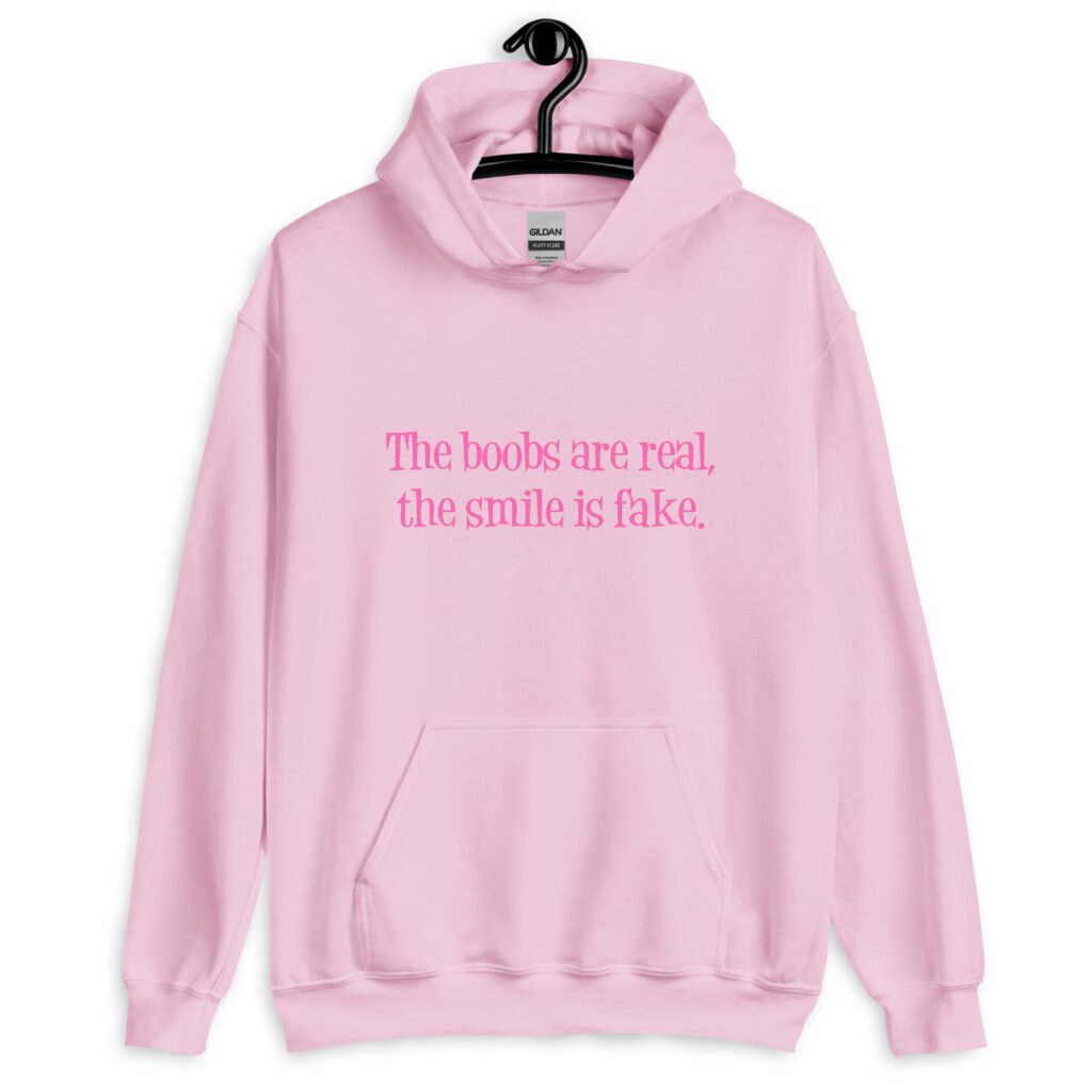 Light pink hoodie sweatshirt with the text 'The boobs are real, the smile is fake.' printed in pink on the front.
