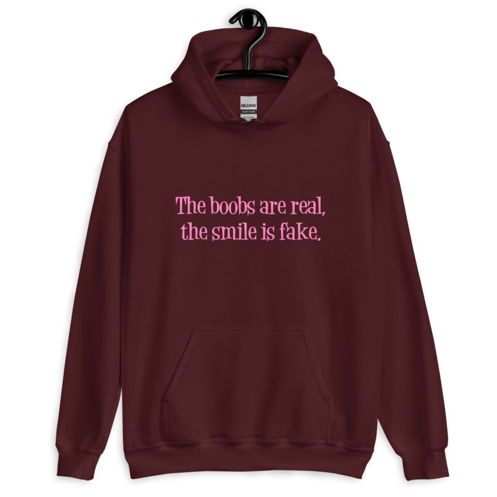 Maroon hoodie sweatshirt with the text 'The boobs are real, the smile is fake.' printed in pink on the front.