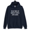 Navy blue hoodie sweatshirt with the funny phrase 'I'm so tired of being my wife's arm candy' printed on the front.