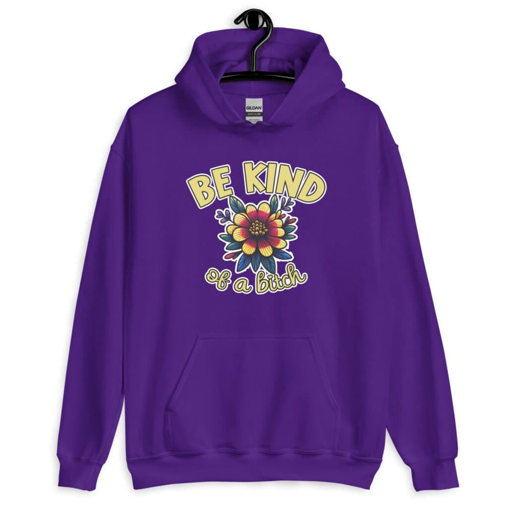 Purple hoodie sweatshirt with an image of a flower and the words Be kind above the flower in yellow bold block font. The words Of a bitch are smaller in script font under the flower. The design is printed on the front.