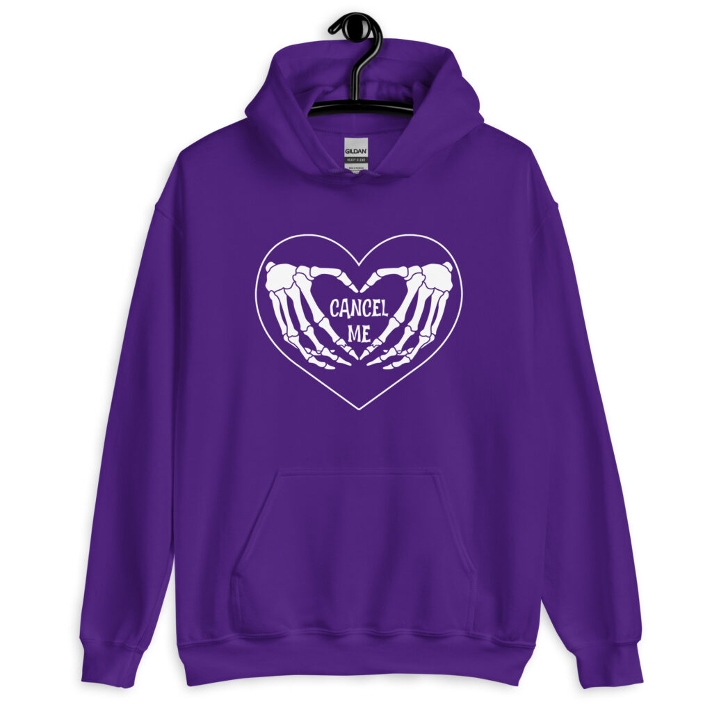 Purple hoodie sweatshirt with a heart and skeleton hands making a heart shape printed on the front. The words 'Cancel Me' are inside of the heart.