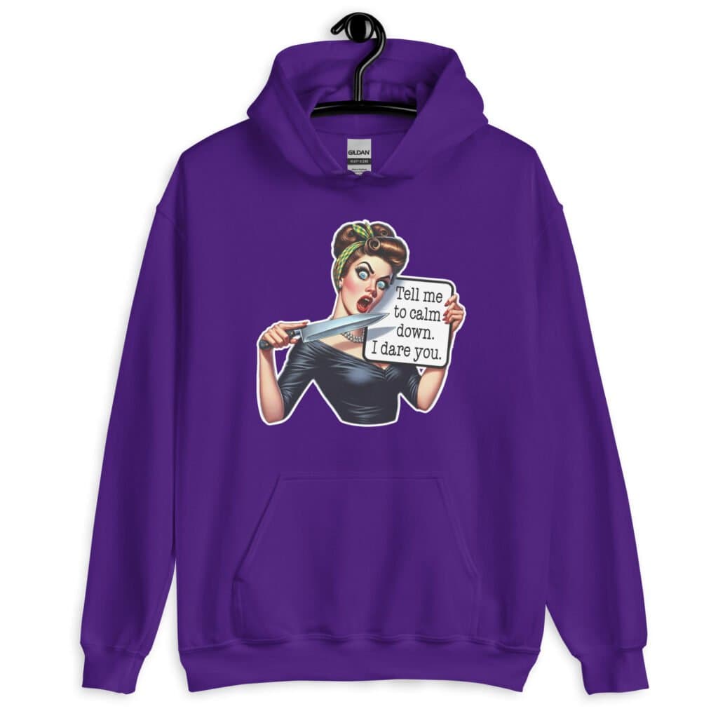 Purple hoodie sweatshirt that has a graphic of an angry looking retro woman holding a knife and a sign. The sign says 'Tell me to calm down. I dare you.' The graphic is printed on the front of the hoodie.
