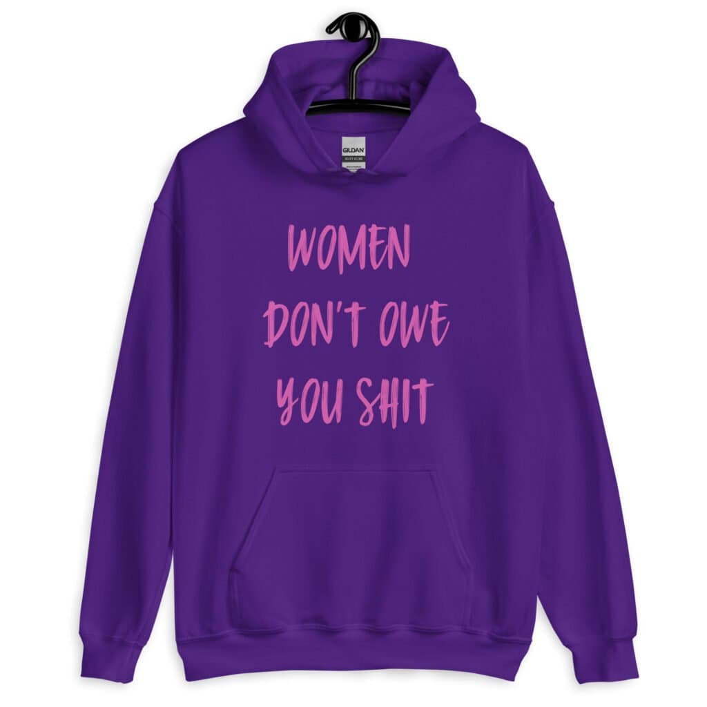 Purple hoodie sweatshirt with the words 'Women don't owe you shit' printed on the front in pink.