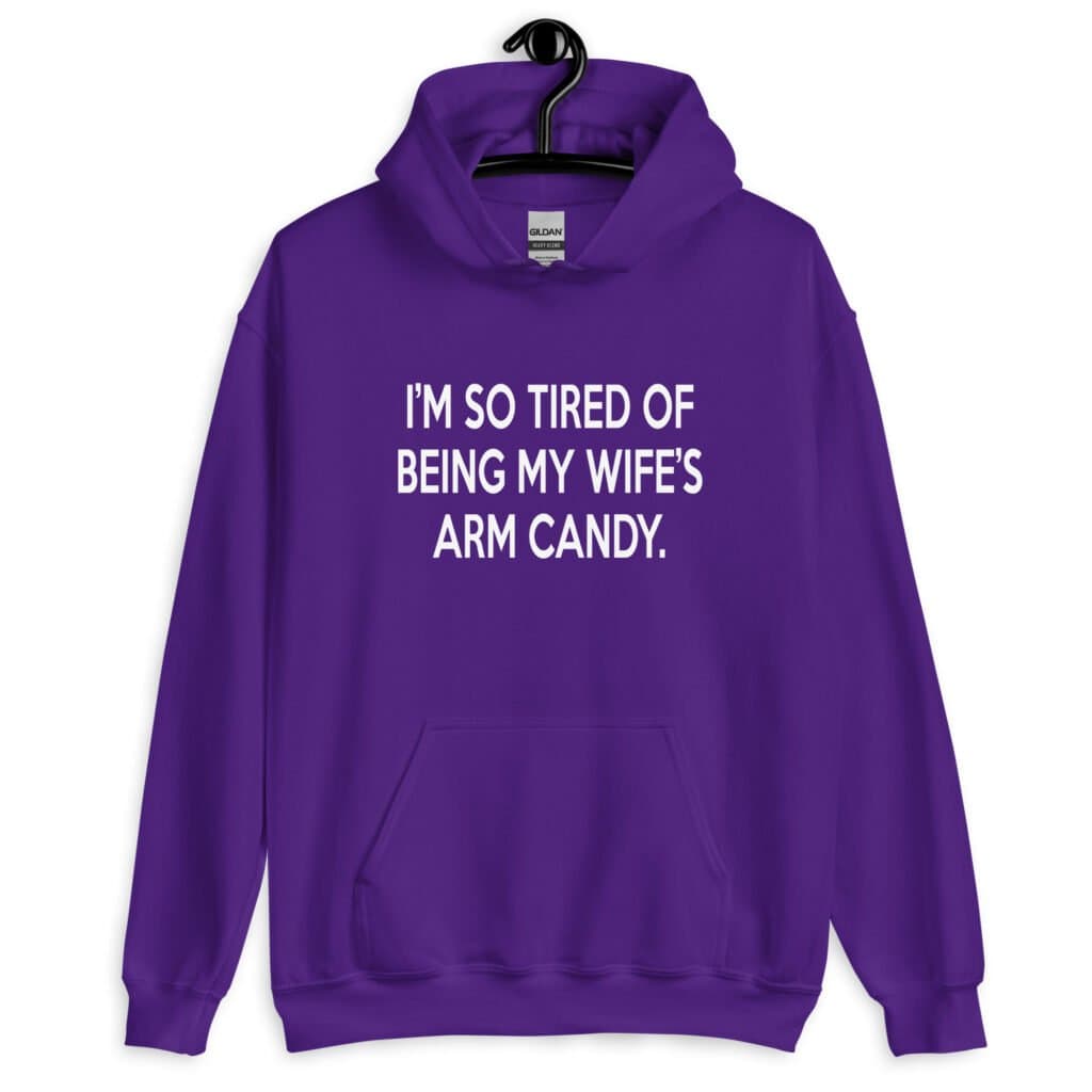 Purple hoodie sweatshirt with the funny phrase 'I'm so tired of being my wife's arm candy' printed on the front.