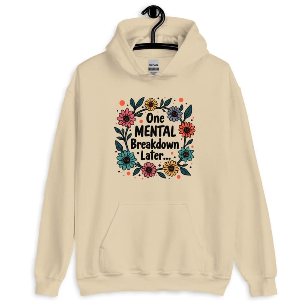 Sand color hoodie sweatshirt with a multi color floral wreath design printed on the front. The words 'One mental breakdown later...' are printed in the center of the wreath.