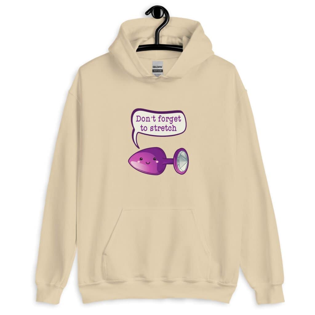 Sand color hoodie sweatshirt that has image of a purple anal plug with a smile face with a speech bubble above with the words 'Don't forget to stretch'. The graphics are printed on the front of the hoodie.