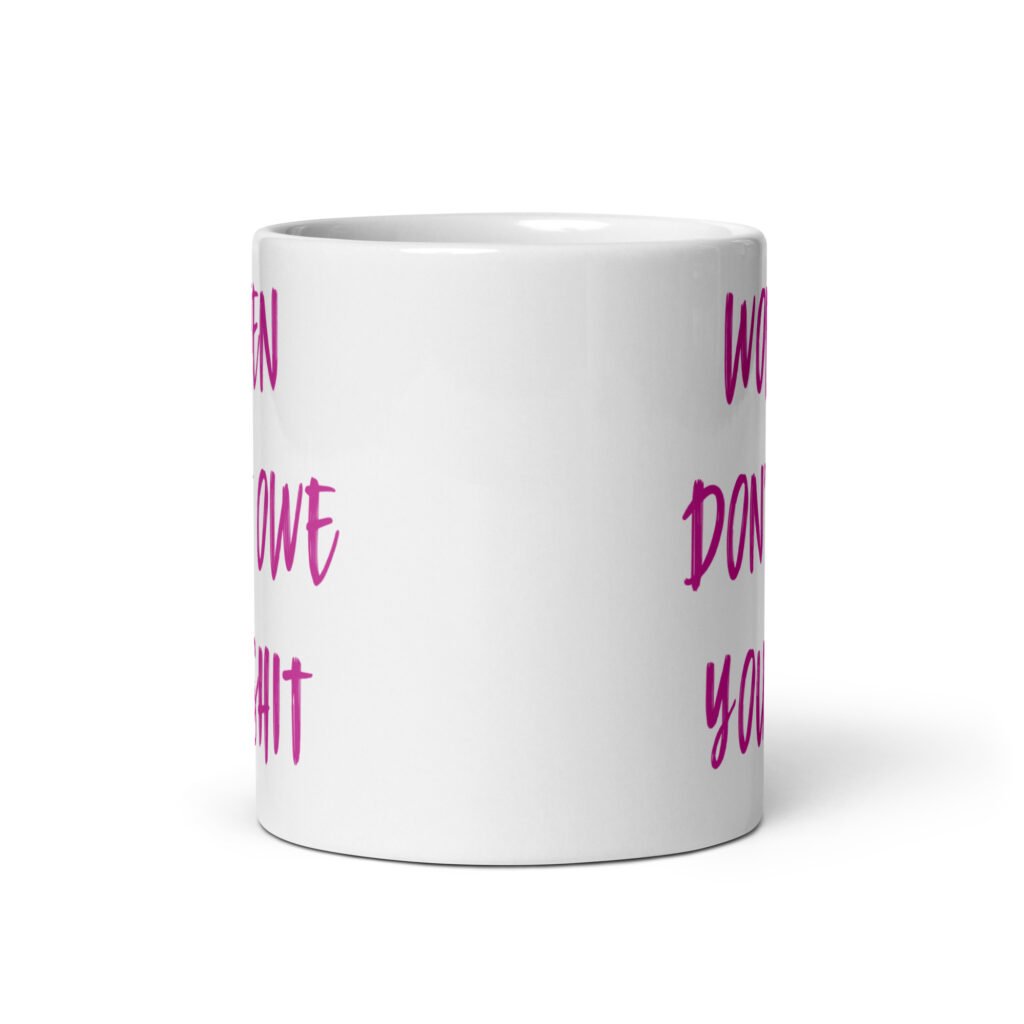 White ceramic coffee mug with the words 'Women don't owe you shit' printed on both sides in pink.