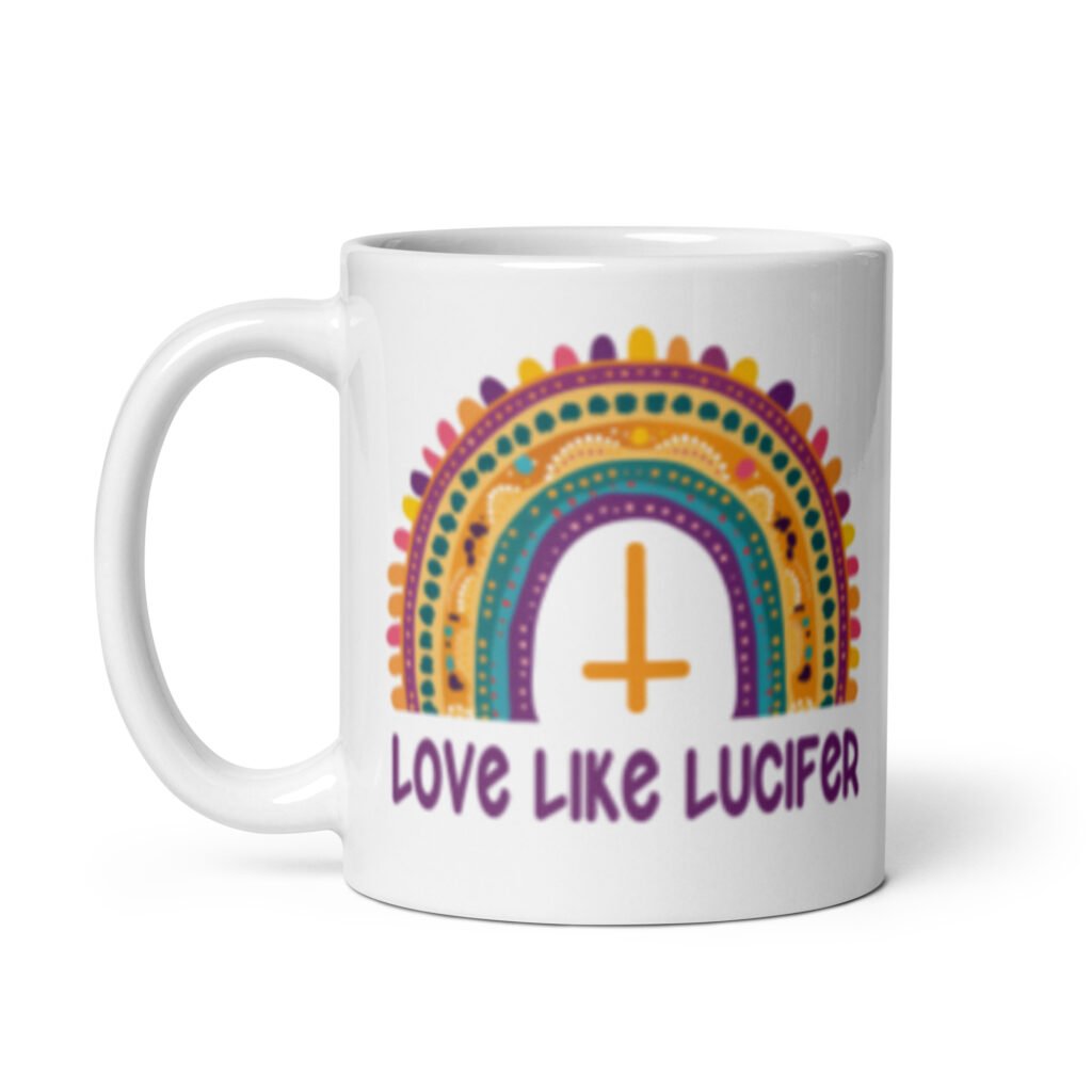 White ceramic mug with an image of a boho style rainbow. There is an upside down cross in the center arch of the rainbow and the text 'Love like Lucifer' printed under. The graphics are printed on both sides of the mug.