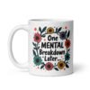 White ceramic mug with a multi color floral wreath design printed on both sides. The words 'One mental breakdown later...' are printed in the center of the wreath.
