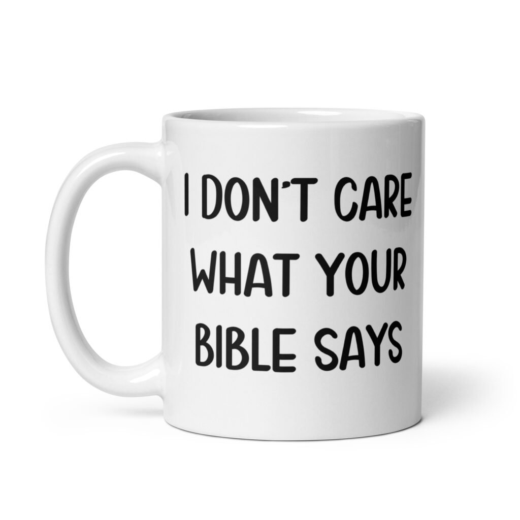 White ceramic coffee mug with the text 'I don't care what your bible says' printed on both sides.