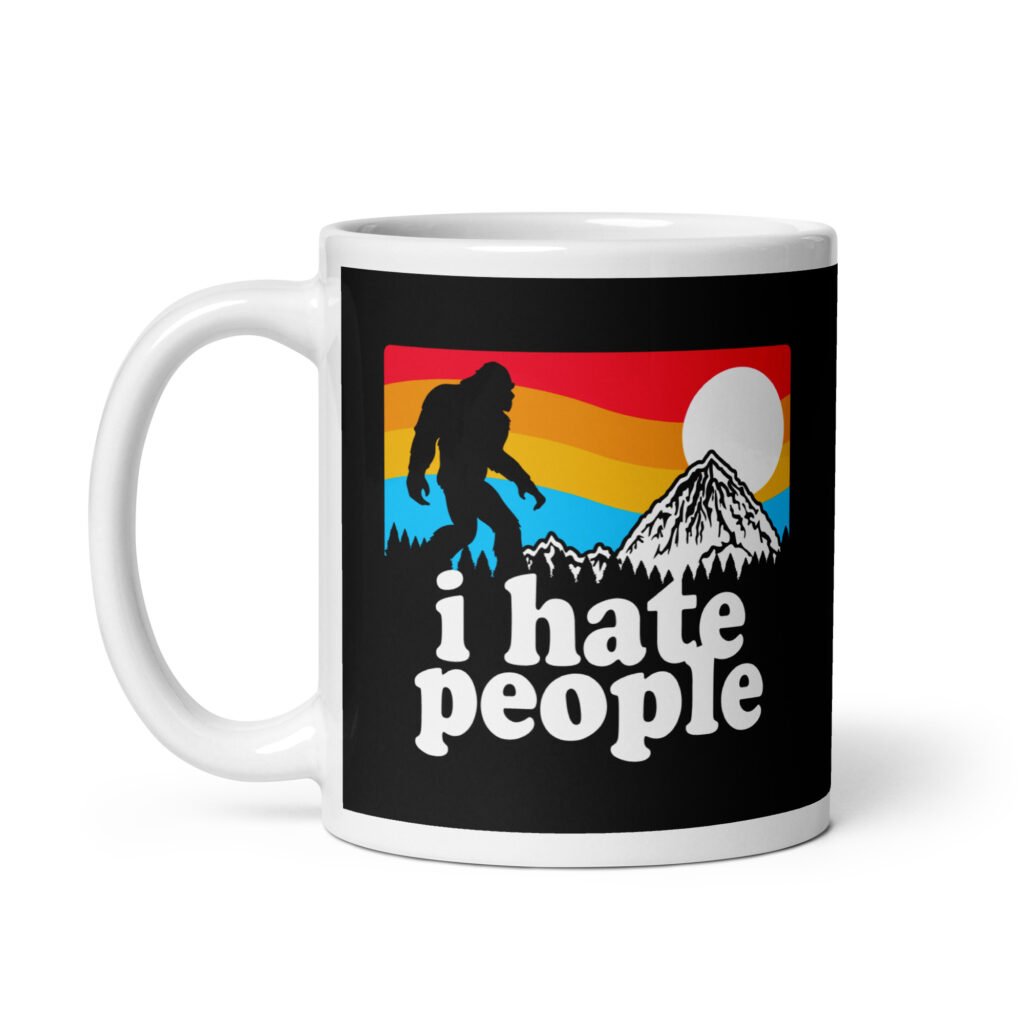 White coffee mug with graphic of Bigfoot walking into the sunset with the text 'I hate people' printed on both sides.