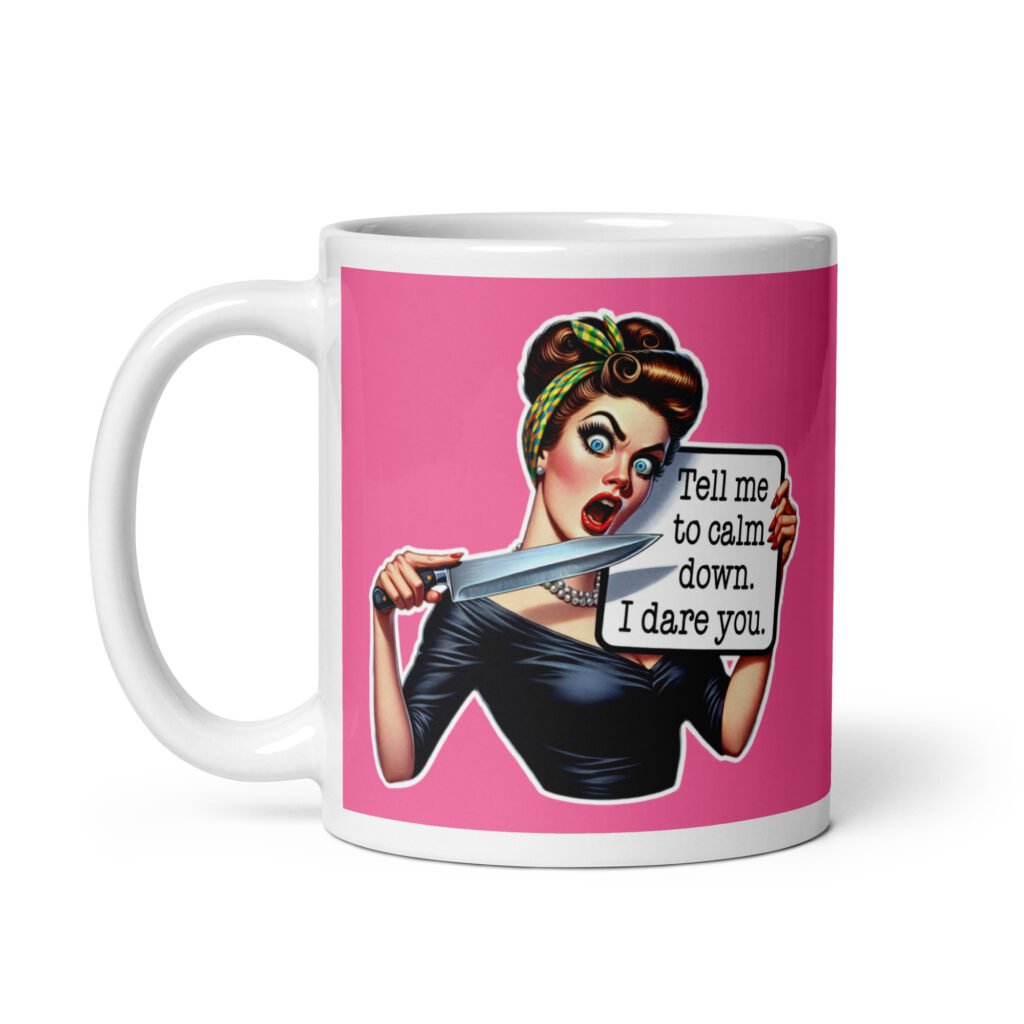 White ceramic coffee mug with pink color wrapped around. The mug has a graphic of an angry looking retro woman holding a knife and a sign. The sign says 'Tell me to calm down. I dare you.' The graphic is printed on both sides of the mug.
