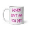 White ceramic coffee mug with the words 'Women don't owe you shit' printed on both sides in pink.