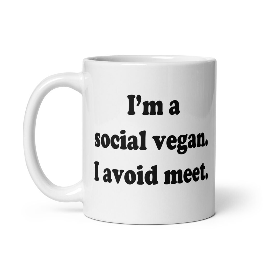 White ceramic mug with the pun phrase 'I'm a social vegan. I avoid meet.' printed on both sides.