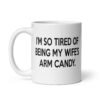 White ceramic coffee mug with the funny phrase 'I'm so tired of being my wife's arm candy' printed on both sides.