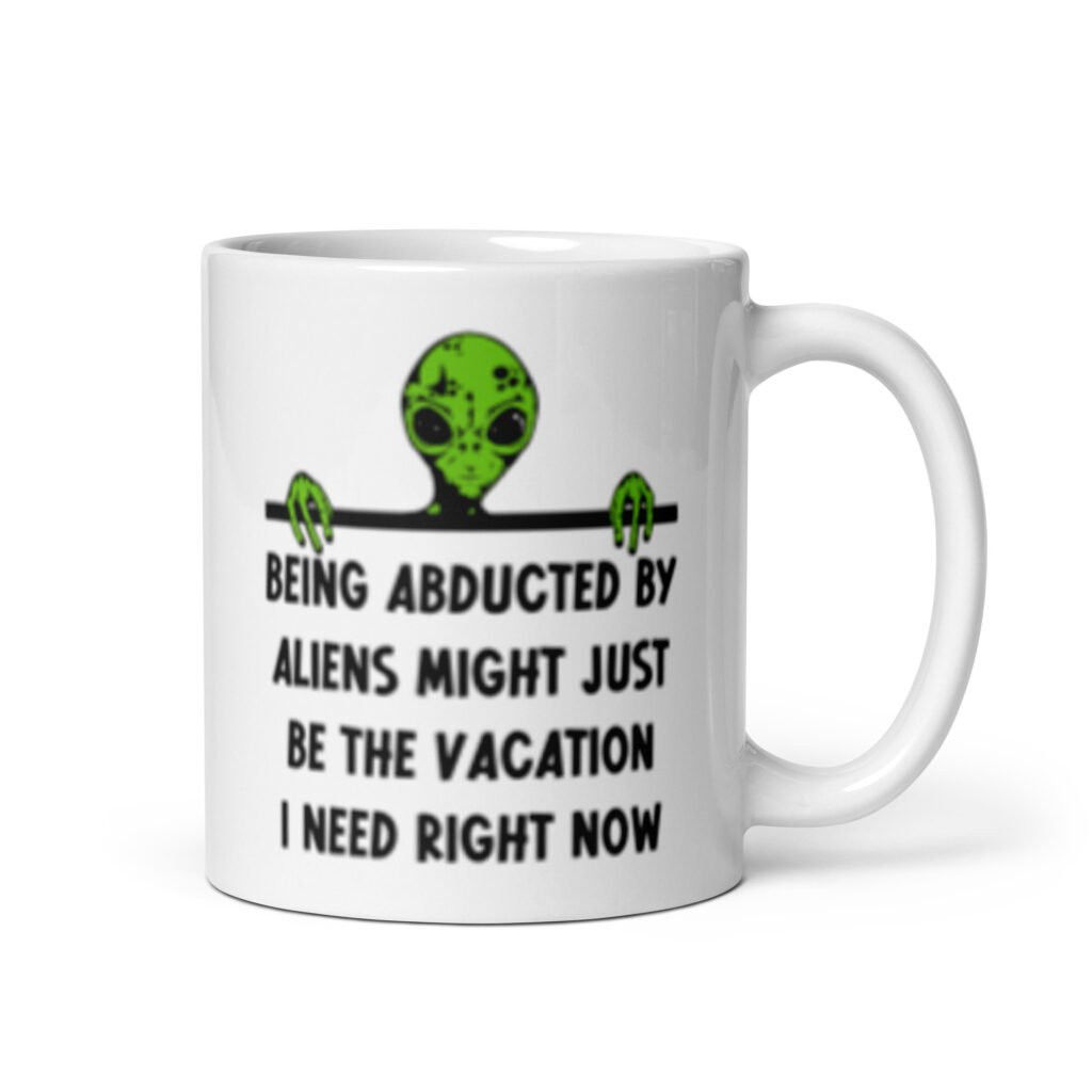 White ceramic mug with image of an alien and the words 'Being abducted by aliens might just be the vacation I need right now' printed on both sides.