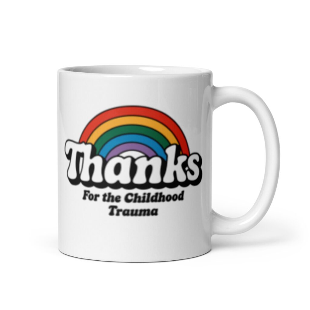 White ceramic mug with an image of a rainbow and the words 'Thanks for the childhood trauma' printed on both sides. The word Thanks is large and the rest of the words are smaller under.