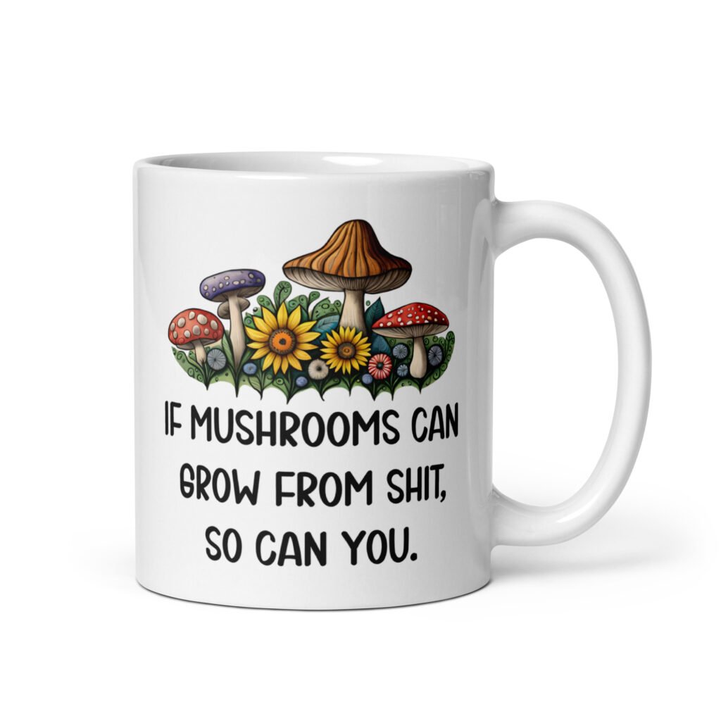 White ceramic coffee mug with images of mushrooms and the text 'If mushrooms can grow from shit so can you' printed on both sides.